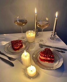 the table is set with two desserts and three glasses of wine, candles, and silverware