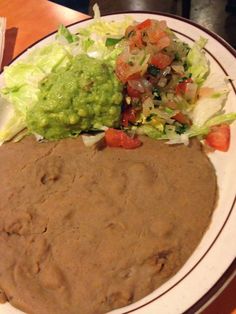 a white plate topped with lettuce, tomato and guacamole next to a salad