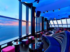 the interior of a restaurant with large windows overlooking the ocean and cityscape at dusk