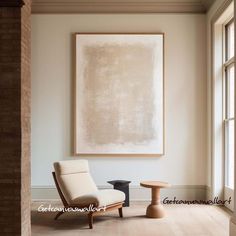 a chair and table in front of a large painting on the wall with windows behind it