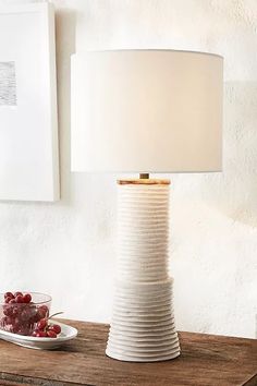 a table lamp sitting on top of a wooden table next to a bowl of fruit