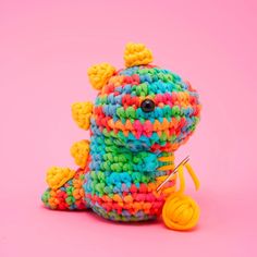 a colorful crocheted stuffed animal sitting next to a pair of scissors on a pink background