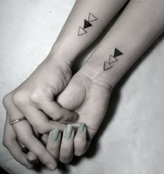 two people holding hands with tattoos on their arms and one has an arrow tattoo on the wrist