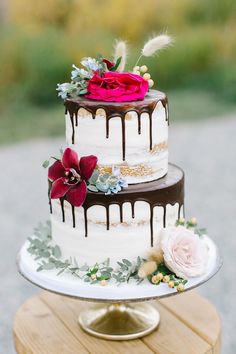 a three tiered cake with flowers and feathers on top is sitting on a wooden table