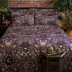 a bed covered in a purple and white bedspread next to a brick wall