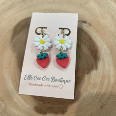 a pair of earrings with flowers on them sitting on top of a wooden table next to a card