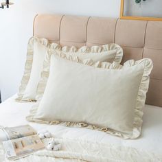 a bed with three pillows and two pictures on the wall above it, along with an open magazine