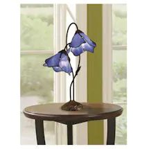 a table with a lamp that has two blue flowers on it and is next to a window