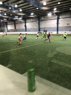 a group of people playing soccer in a large room with green grass on the floor