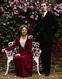 an older woman sitting on a white bench next to a young man in a suit