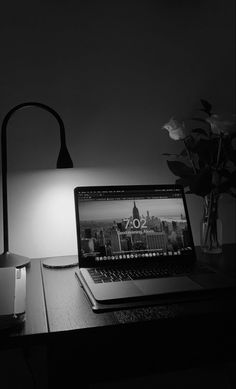 a laptop computer sitting on top of a desk next to a lamp and vase with flowers