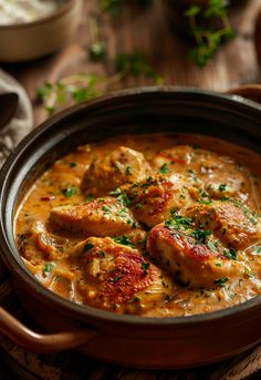 a bowl filled with chicken and cheese soup on top of a wooden table next to bread