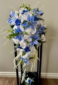 a bouquet of blue and white flowers sitting on a black stand next to a wall