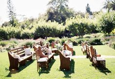 an outdoor seating area with wooden benches and chairs in the middle of it, surrounded by greenery