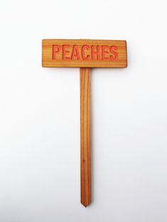 a wooden sign with the word peaches on it hanging from a wall next to a white wall