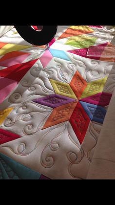 a quilted table topper with colorful designs on it and a black object in the middle