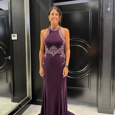 a woman standing in front of a black door wearing a purple dress with an embellishment on it