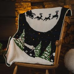 a knitted christmas blanket sitting on top of a wooden chair next to a fire place