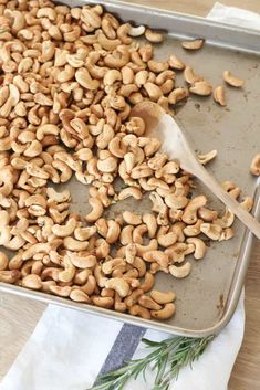 roasted cashews on a baking sheet with a wooden spoon and rosemary sprig