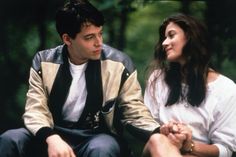 a young man and woman sitting next to each other in the woods looking at each other