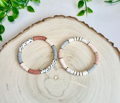 two bracelets sitting on top of a piece of wood next to green plants and leaves