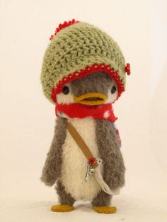 a small stuffed penguin wearing a knitted hat and scarf with a brown leather strap