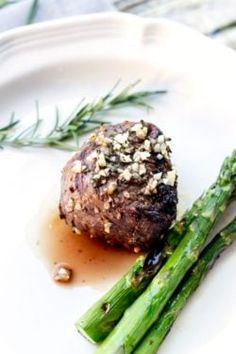 a piece of meat and asparagus on a white plate with some garnish