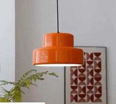 an orange lamp hanging from a ceiling next to a potted plant in a living room