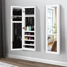 a white mirrored wall mounted jewelry cabinet next to a window with a mirror on it