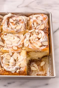 a pan filled with cinnamon rolls covered in icing and almonds on top of a marble counter