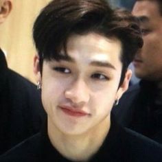 a young man with dark hair and piercings standing in front of other men wearing black shirts