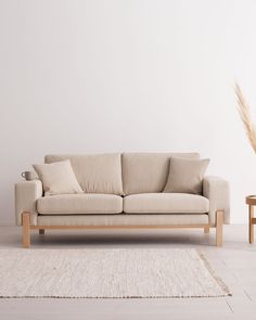 a beige couch sitting on top of a white rug next to a wooden coffee table