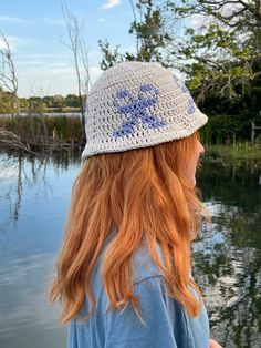 a woman with long red hair wearing a crocheted hat looking out over the water