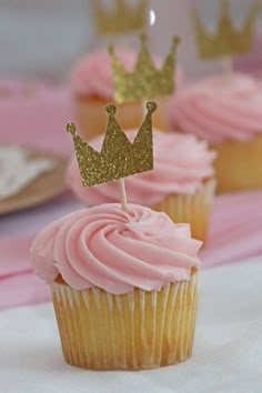 cupcakes with pink frosting and gold crowns on top are sitting on a table