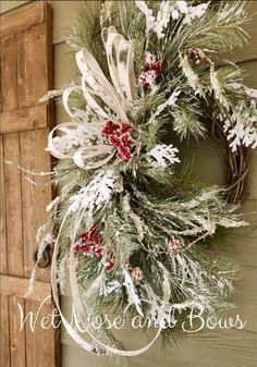 a christmas wreath hanging on the side of a building with snow and evergreens around it