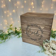 a wooden box sitting on top of a table next to some flowers and greenery