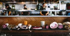 meats are lined up on a counter in a restaurant with people working behind them