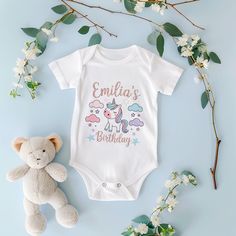 This specially designed unicorn themed 1st birthday bodysuit can be personalized in pastel tones. It is compatible with the most popular themes in the USA with the text 'Emilia's 1st Birthday'. Unicorn themed 1st birthday bodysuit is one of the most preferred birthday concepts for girls in the USA. This design, decorated with unicorns and stars in pastel colors, offers a simple yet striking aesthetic. It can be personalized with the phrase 'Emilia's 1st Birthday' in a handwritten style. It is a Customizable Cute Birthday Bodysuit, Customizable Cute Bodysuit For Birthday, Personalized Pink Onesie For Birthday, Cute Personalized Onesie For Birthday, Customizable Cute Onesie For Birthday, Cute Birthday Bodysuit With Name Print, Cute Custom Print Birthday Onesie, Cute Birthday Onesie With Custom Print, Customizable White Onesie For Birthday