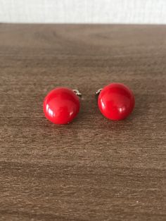 two red earrings sitting on top of a wooden table