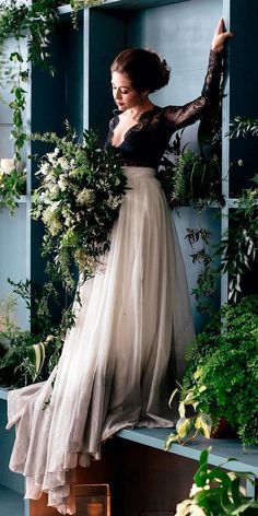 a woman in a long dress standing on a shelf with flowers and greenery behind her