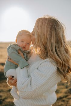 a woman holding a baby in her arms and kissing it with the sun behind her