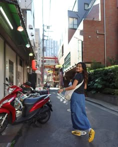 a woman standing on the side of a street next to a red scooter