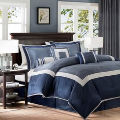 a bed with blue and white comforters in a room next to a lamp on a table