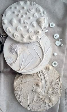 three ceramic plates sitting on top of a table covered in buttons and other things to make it look like they are made out of clay