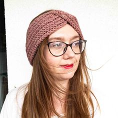 a woman wearing glasses and a knitted headband is looking at the camera while standing in front of a white wall