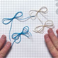 two hands holding blue string on top of a piece of paper