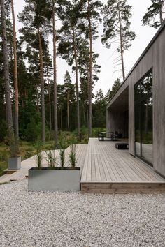 a wooden deck surrounded by tall pine trees and graveled area with benches on it