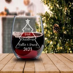 a wine glass sitting on top of a wooden table next to a christmas tree and pine cones