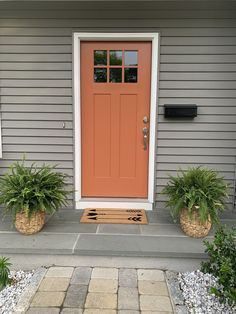 the front door is painted orange and has two planters