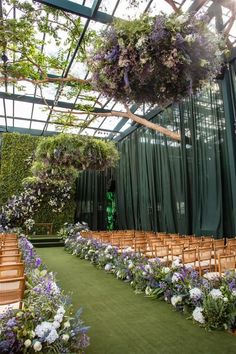 an indoor ceremony setup with chairs and flowers on the aisle, greenery hanging from the ceiling